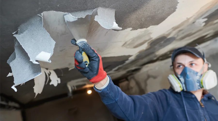 Worker removing damaged ceiling material during commercial fire damage restoration, wearing protective gear and focused on cleanup process.