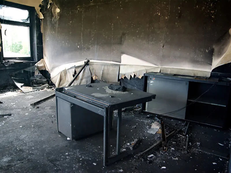 Fire-damaged interior with charred walls, debris, and a scorched table, illustrating the need for fire and smoke damage restoration services.