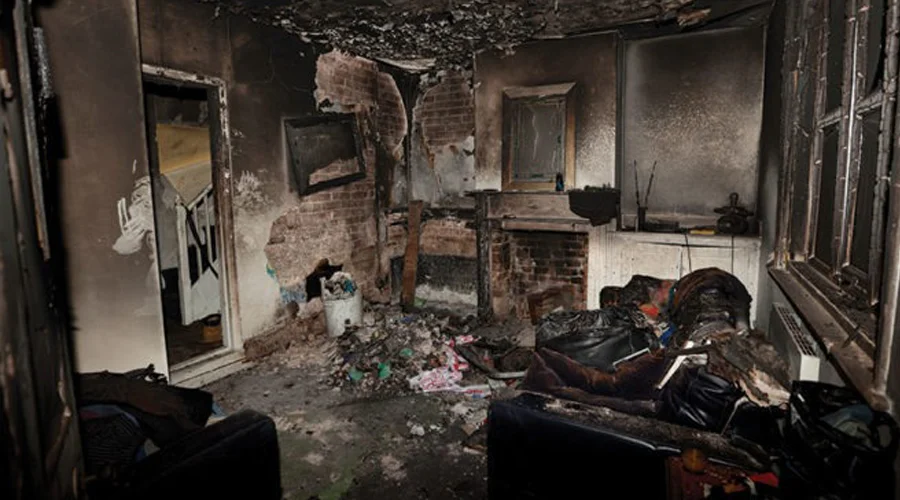 Burned interior of a residential room showing severe fire damage, with charred walls, debris, and damaged furniture, highlighting the need for professional fire and smoke damage restoration services.