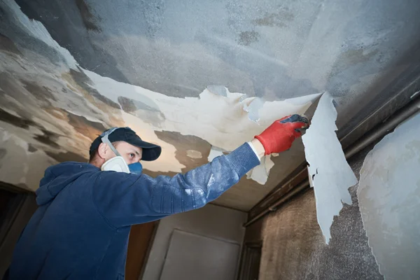 Worker removing damaged ceiling material during fire and smoke damage restoration process.