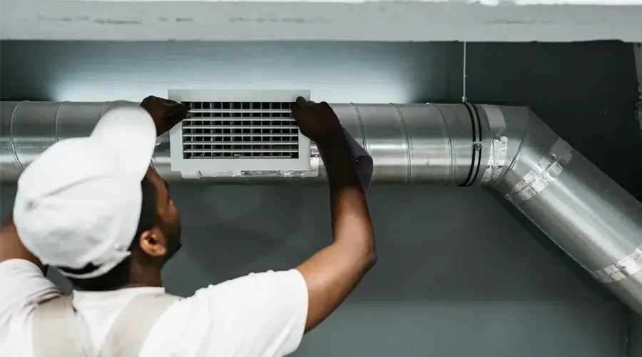Technician performing commercial air duct cleaning, adjusting vent cover, ensuring indoor air quality improvement for business environments.