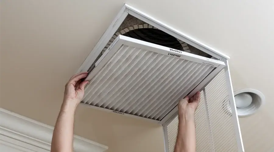 Person replacing air filter in ceiling vent, emphasizing maintenance for commercial air duct systems and indoor air quality.