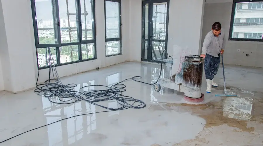 Worker using a floor scrubber in a commercial space undergoing water damage restoration, with cleaning equipment and hoses visible.