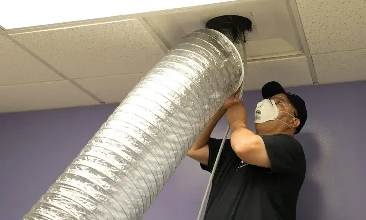 Technician wearing a mask inspecting a silver air duct in a ceiling