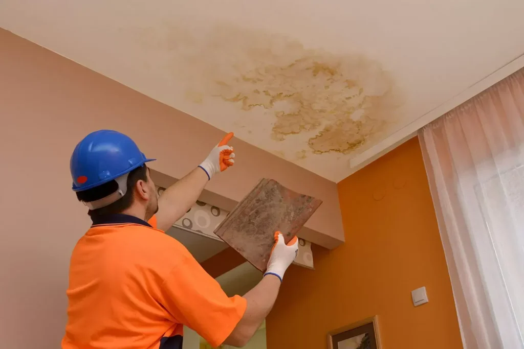 Worker inspecting water damage on ceiling, wearing safety gear and gloves