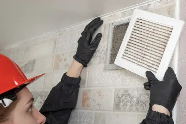 Technician in a red helmet replacing a wall air vent filter